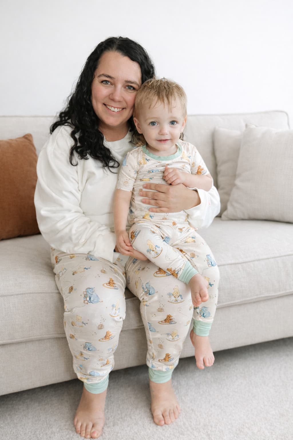Woman and child sitting on a couch wearing matching bamboo pajamas with classic Pooh patterns.